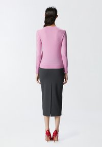 Roze rebrasti dugi rukav gornji dio u kombinaciji sa sivom uskom midi suknjom koja ima prorez straga; model nosi crvene štikle.