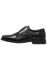 Black leather dress shoe with smooth texture, round toe, five-eyelet lace-up design, and a low-profile black sole with a red accent.
