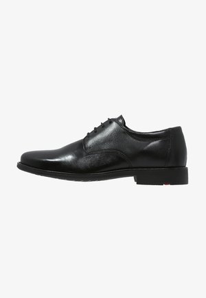 Chaussure habillée en cuir noir avec une texture lisse, bout arrondi, design à lacets à cinq œillets et une semelle noire basse avec une touche de rouge.