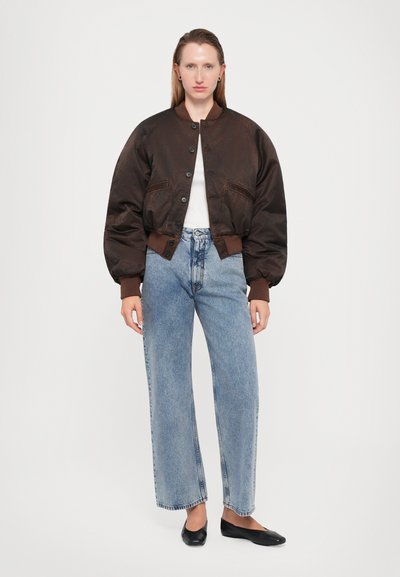 Brown bomber jacket with a round collar, buttons, and oversized sleeves. Paired with high-waisted light blue jeans and black flats.