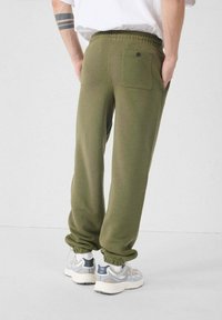 Olijfgroene joggingbroek van zachte stof, met een elastische tailleband, klein geribbelde enkels en een achterzak met een zwarte knoop.