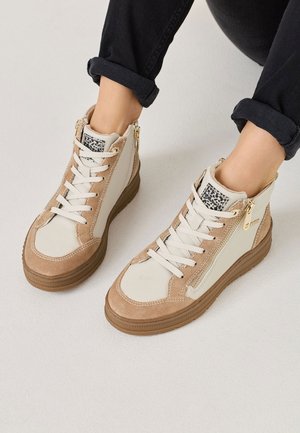 Hoge sneakers in crème en tan suede met metalen rits, ronde neus, contrasterende veters en rubberen zool. Textuur op de zijpaneel.