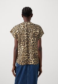 Top a maniche corte con stampa leopardata in una palette di colori beige e marrone, caratterizzato da una vestibilità ampia e scollo rotondo. Il tessuto sembra leggero.