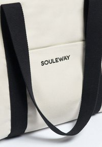 Bílá plátěná taška přes rameno s černými látkovými popruhy, s přední kapsou označenou "SOULEWAY." Materiál má hladkou texturu.