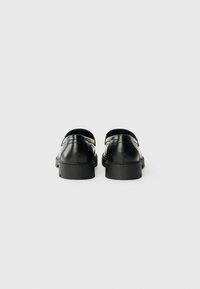 Black leather shoes with a low profile, smooth texture, and thick rubber soles. Features minimal design with no visible hardware or accents.