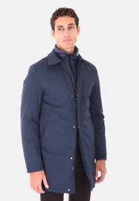 Cappotto impermeabile blu navy con colletto, chiusura con zip e dettagli con bottoni a pressione. Include tasche laterali e un interno liscio.