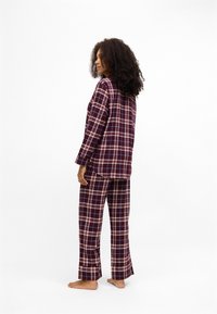 Σετ πυτζάμα σε κόκκινο και ναυτικό καρό, κατασκευασμένο από μαλακό ύφασμα, που διαθέτει μπλούζα με μακριά μανίκια και ταιριαστά παντελόνια με χαλαρή εφαρμογή και λεπτομέρειες στο στρίφωμα.