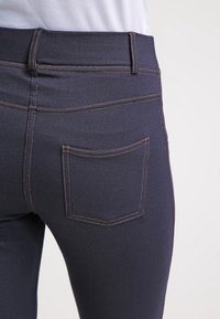 Mörkblå denimjeans med rak passform, bakfickor och kontrasterande orange sömmar längs sömmarna. Slät textur, tight passform.