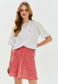 Bílý bavlněný tričko s krátkým rukávem a barevnými vyšitými detaily na hrudi, spárováno s korálovou sukní se květinovým vzorem.