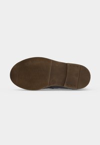 Semelle d'une chaussure marron foncé avec talon texturé et zone avant du pied rainurée, taille 25 marquée près du centre.