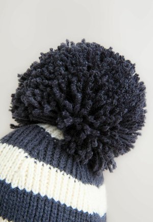 Berretto lavorato a maglia con strisce marine e crema, caratterizzato da un grande pon-pon in tessuto navale sulla parte superiore. Materiale morbido in misto lana.