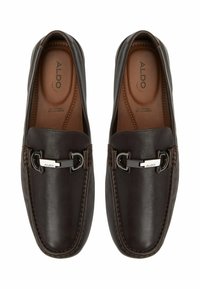 Mørkebrune læder loafers med en glat overflade, prydet med sølvfarvet hardware og dekorativ søm langs kanterne.