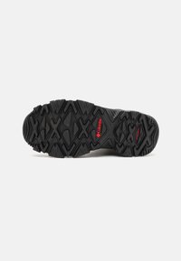Semelle de chaussure extérieure noire avec un motif robuste, dotée de crampons multidirectionnels pour une meilleure traction et d'un accent de logo rouge.