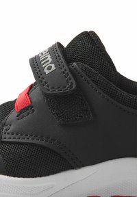 Czarne buty sportowe z siateczkowymi panelami, rzepem i czerwonymi akcentami. Mają białą podeszwę o teksturowanej powierzchni z kontrastowymi szwami.