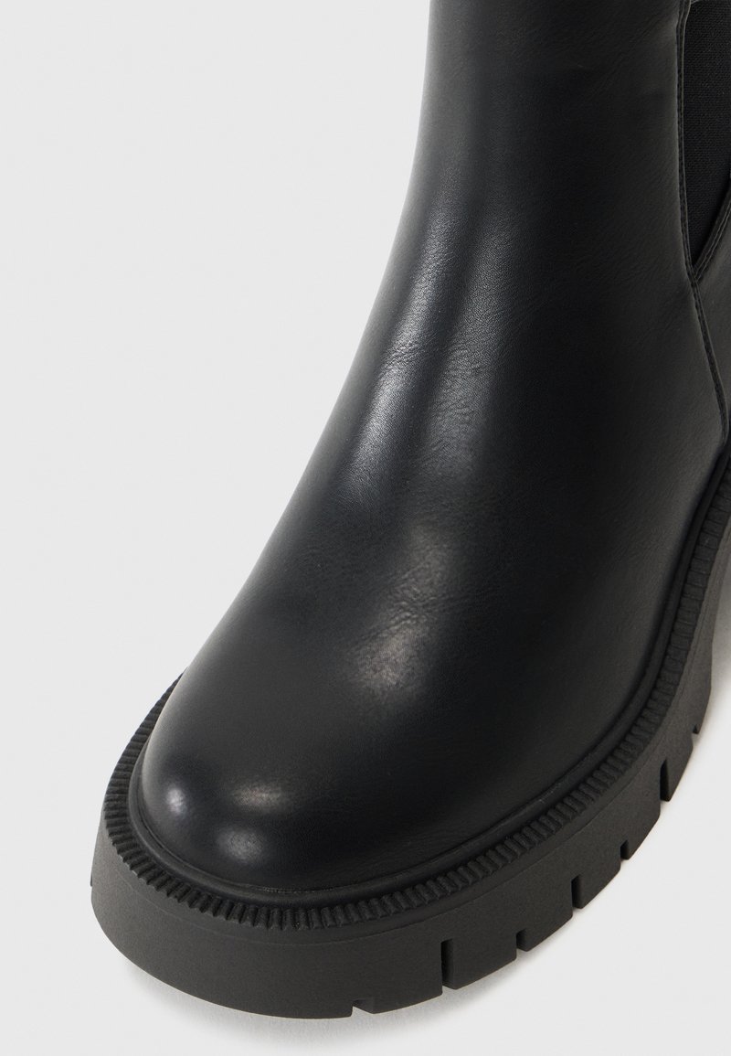Stivale alla caviglia in pelle nera con finitura liscia, suola in gomma nera spessa con battistrada e pannelli laterali elastici per facilitare l'indossamento.