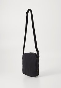 Černá křížová taška vyrobená z nylonu, se stylovým obdélníkovým tvarem, nastavitelným popruhem a neonově žlutými švy. S vrchním zipovým uzávěrem.