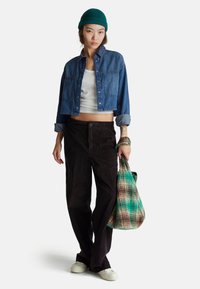 Džínová zkrácená bunda, bílý top, hnědé manšestrové kalhoty, béžové tenisky, držící duhovou kostkovanou tašku. Obsahuje texturované materiály.