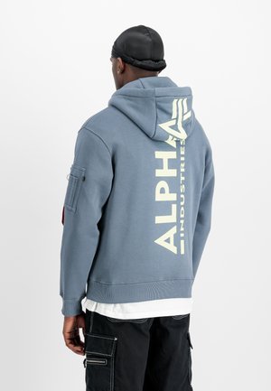 Blaues Hoodie aus Baumwollmischung. Auf der Rückseite befindet sich ein großes "ALPHA INDUSTRIES"-Logo in Creme und eine Reißverschlusstasche am Ärmel.