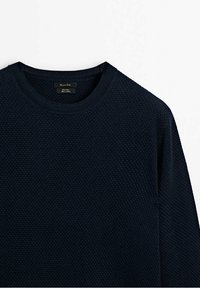 Pull ras-du-cou en maille texturée bleu marine avec manches longues et une petite étiquette en tissu à l'intérieur du col.