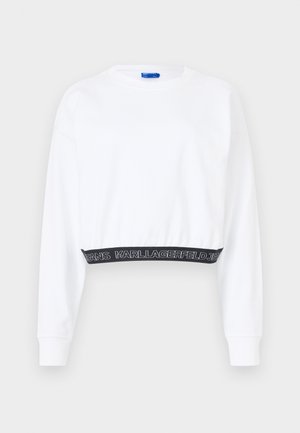 Bela skrajšana majica s dolgimi rokavi, z rebrastim zaključkom in črnim pasom, na katerem je v beli barvi napis "KARL LAGERFELD JEANS". Gladka tekstura.