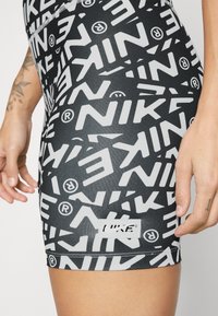 Lähikuva henkilöstä, jolla on yllään mustat shortsit, joissa on rohkeat, valkoiset Nike-logo-kuviot ja näkyvä pieni Nike-tarra helman lähellä.