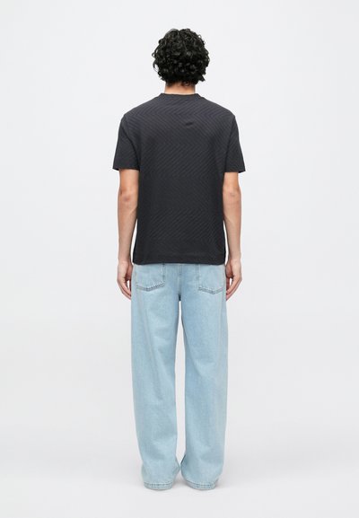 Čierne tričko s krátkym rukávom s chevronovým vzorom, v kombinácii s bledomodrými nohavicami s širokými nohavicami. Tkanina pôsobí mäkko a neformálne.