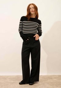 Czarny i biały sweter w paski o żebrowanej teksturze, zestawiony z wysokim stanem czarnymi szerokimi spodniami i czarnymi butami.