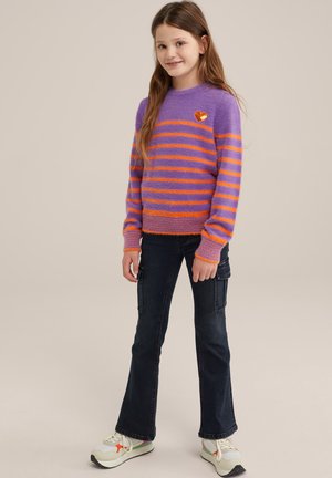 Maglione a strisce viola con strisce arancioni, texture pelosa, collo rotondo e toppe a forma di cuore. Abbinato a jeans scuri e scarpe da ginnastica multicolori.
