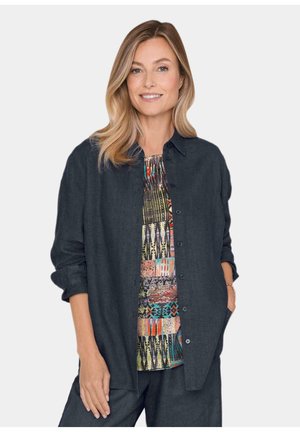 Donkergrijze button-up blouse met opgerolde mouwen over een multikleurige top met een patroon dat uit geometrische en abstracte ontwerpen bestaat.