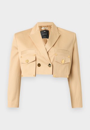 Blazer beige court avec manches longues, larges revers, deux poches à rabat à l'avant avec boutons dorés, et fermeture à double bouton doré.