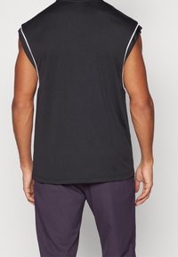 Black sleeveless athletic top with white trim, made of smooth fabric. Features a round neckline and relaxed fit. Worn with dark purple pants.
