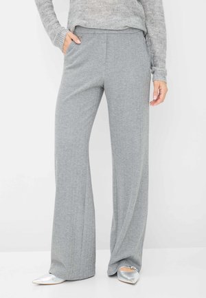 Pantalons larges en chevrons gris avec poches latérales et texture lisse, associés à des chaussures argentées à talons pointus.