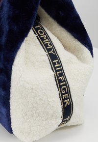 Sac fourre-tout en tissu sherpa bleu marine et blanc avec une bandoulière noire et un texte doré "Tommy Hilfiger".