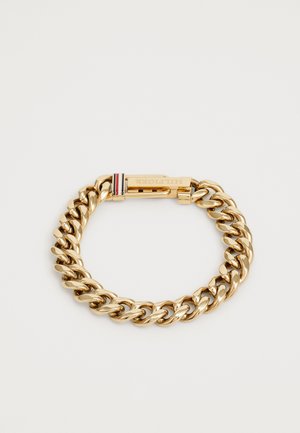 Gullfarget kjede armbånd med tykke, sammenkoblede lenker og en sikker lås. Inkluderer en subtil merkenota i rødt, hvitt og blått.