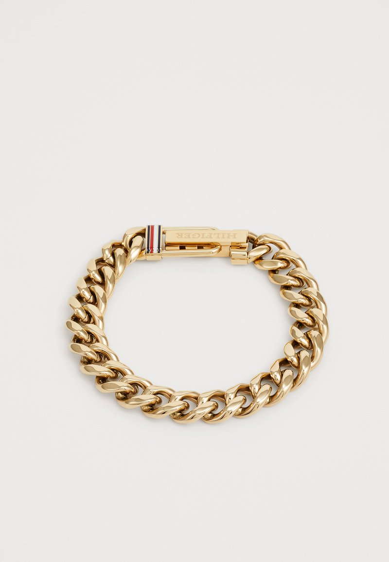 Pulsera de cadena en tono dorado que presenta eslabones gruesos entrelazados y un cierre seguro. Incluye un sutil acento de marca en rojo, blanco y azul.