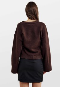 Brązowy sweter z dzianiny o luźnym kroju, z opuszczonymi ramionami i ściągaczami, w połączeniu z czarną dopasowaną spódnicą.