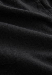 Sort stof med en glat tekstur, der har fine, subtile vævede mønstre. Overfladen virker let reflekterende enkelte steder.