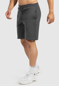 Shorts en coton gris avec une taille élastique et un cordon de serrage, dotés de deux poches latérales et d'une coupe régulière. Portés avec des baskets blanches.