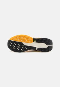 Semelle de chaussure avec un design en caoutchouc noir et jaune, présentant un motif texturé pour l'adhérence et une semelle intermédiaire blanche pour le confort.