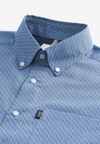 Camicia button-up azzurro chiaro con un motivo testurizzato, due bottoni sul colletto e una tasca a toppa. Presenta una piccola etichetta con logo nera.