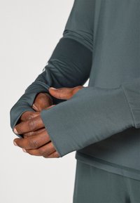 Αθλητικό πουκάμισο μακρύ μανίκι από μαλακό θαλασσί ύφασμα. Διαθέτει τρύπες για τον αντίχειρα στους καρπούς και έχει απαλή υφή με εφαρμοστή σχεδίαση.