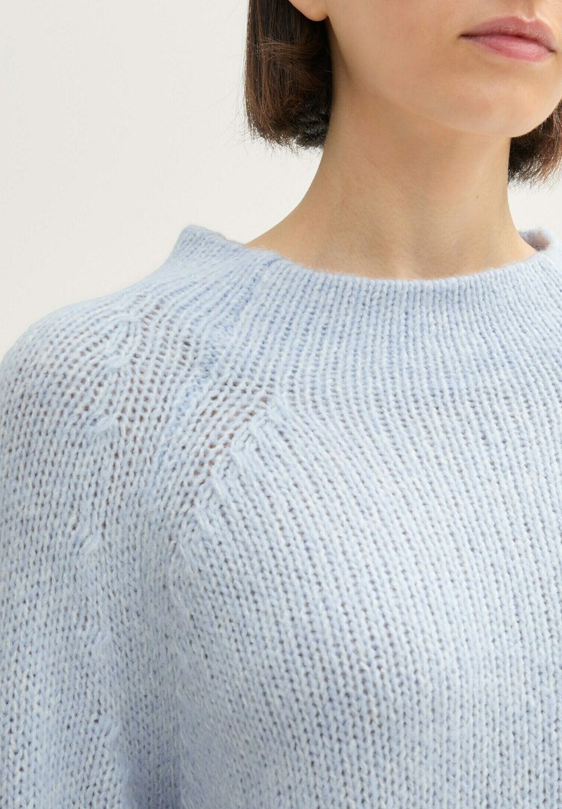 Jasnoniebieski sweter dzianinowy z szerokim dekoltem i detailem w warkocz na ramionach, o miękkiej i lekko prześwitującej fakturze.