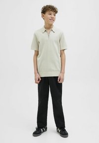 Ljusgrå kortärmad polo med dragkedja i halsen och ribbade kanter, matchad med svarta byxor med knäpaneler och svarta sneakers.