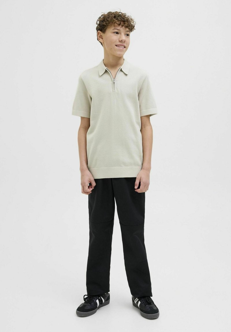 Ljusgrå kortärmad polo med dragkedja i halsen och ribbade kanter, matchad med svarta byxor med knäpaneler och svarta sneakers.