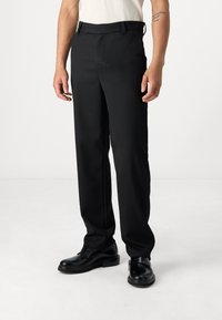 Schwarze, maßgeschneiderte Hosen mit geradem Schnitt, ausgestattet mit Seitentaschen und einer glatten Textur, kombiniert mit schwarzen Dressschuhen.