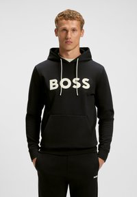 Juodas džemperis, pagamintas iš minkštos medžiagos, su dideliu baltu "BOSS" logotipu, su raišteliais ir kengūros kišene. Lygus paviršius ir laisvas siluetas.
