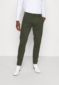 Gröna bomullbyxor med slim fit, med knappstängning och sidofickor. Matchas med vita sneakers.