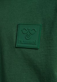 Grønne bomulds t-shirt med et struktureret grønt gummilogo patch med ordet "hummel" og et særpræget mønsterdesign.