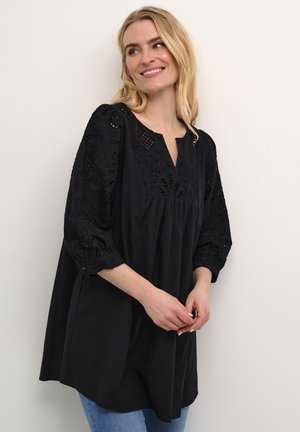 Sort tunika med intrikate blonde detaljer på ærmerne, v-hals og flydende silhuet. Korte puffede ærmer med elastiske manchetter og letvægtsstof.