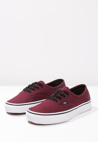Bordeaux canvas sneakers met zwarte veters, witte rubberen zool, zwarte accenten en ronde neusontwerp. Klassiek low-top silhouet.